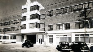 A grayscale picture of 1942, of a building and ancient cars parked in front of it.