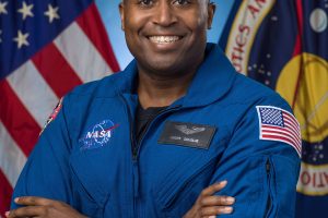 A head of Andre Douglas wearing NASA uniform with the US flag and NASA flag in the background behind him.