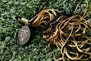 Johns Hopkins University logo engraved on a oval shape metal, attached to a black and yellow tassel, which is kept on the grass.