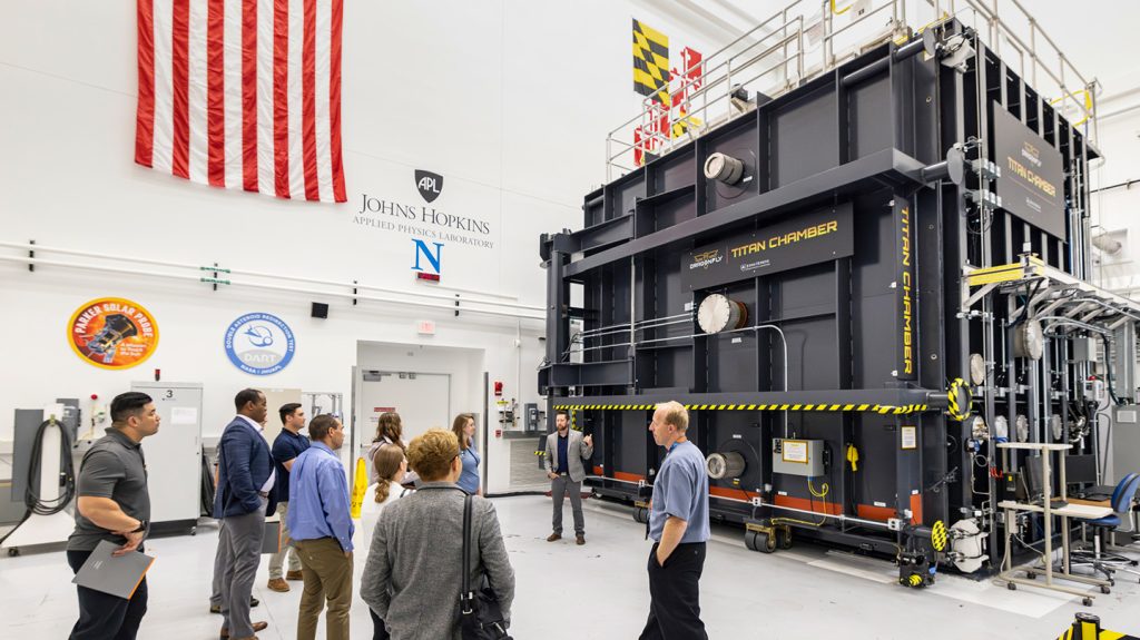 Students look at a large, black rectangular chamber inside a lab. 