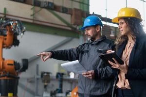 Two engineers in hard hats inspect a machine.