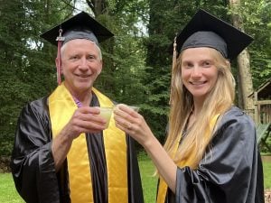 Don Grage and Casey Qadir in a backyard, in graduation regalia, toasting.