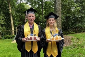 Don Grage and Casey Qadir in a backyard, in graduation regalia holding graduation cakes.