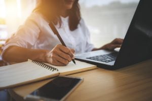 young woman looking at laptop and writing in notebook