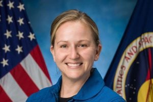 Rebecca Lawler's official NASA photo, wearing a blue jumpsuit with a backdrop of U.S. flag and NASA flag