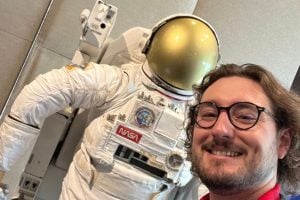 image of a man wearing glasses standing in front of a space suit