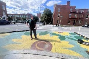 image of man standing in the middle of a sunflower mural that is painted on the street